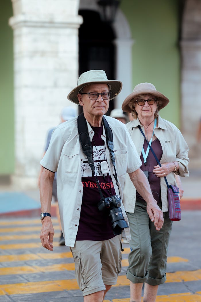 services-03 Elderly couple with sun hats and cameras crossing a zebra crossing outdoors.
