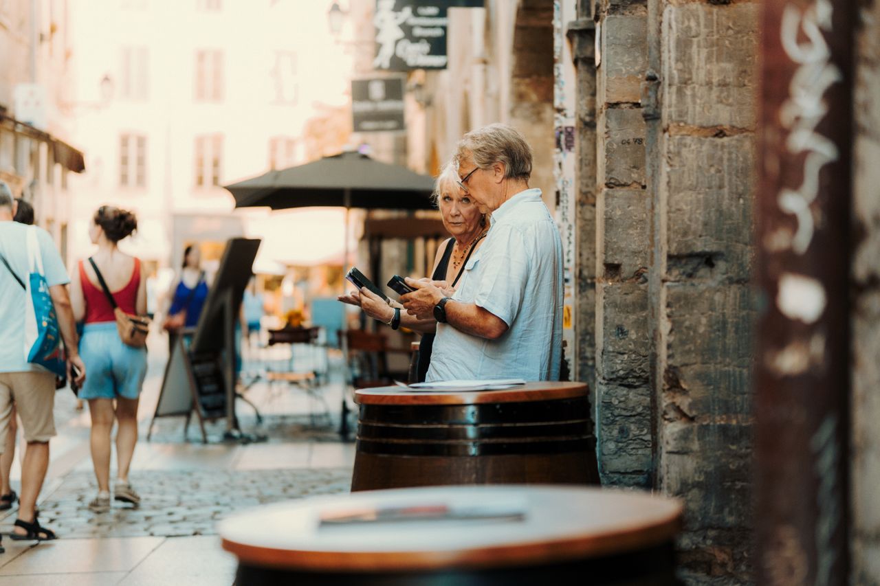 hero-img A senior couple examines their surroundings in a quaint European street setting.